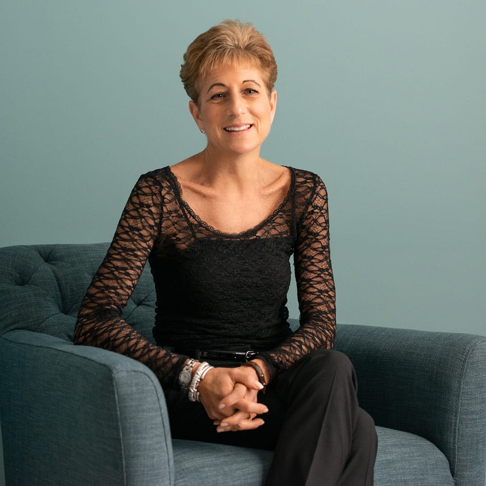 Marcy Lehman Seated in a blue chair wearing a black dress