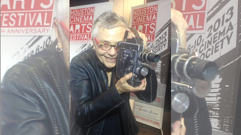 Barbara Hammer in front of a movie poster holding a film camera