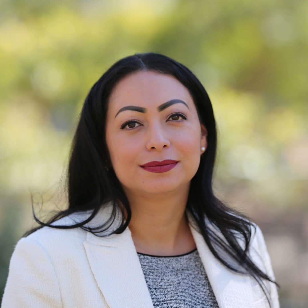 Anna Romero professional headshot. She is wearing a white blazer and a gray shirt underneath