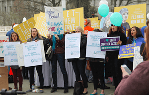 A crowd stands outside with signs