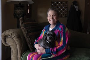 Deb Robertson sits with her dog on her lap. They both are looking toward the camera.