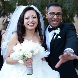 Ana and Juan Romero smiling on their wedding day. Ana wears her wedding dress and holds a bouquet of white flowers. Juan is in a black tuxedo.