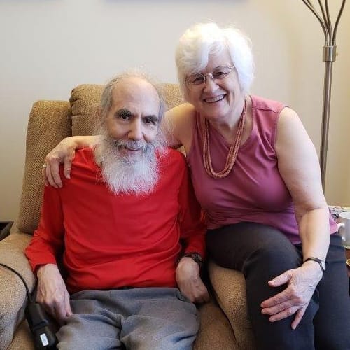 Celia and Bob Morris sit together on a chair smiling at the camera.