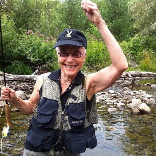 Barbara Hammer posing in a river holding a fishing pole