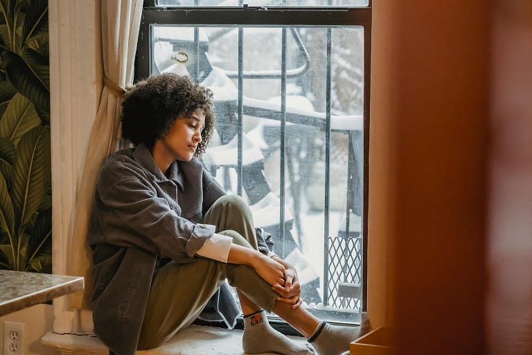 A woman sits in the window looking forlorn. The world outside is snowy.