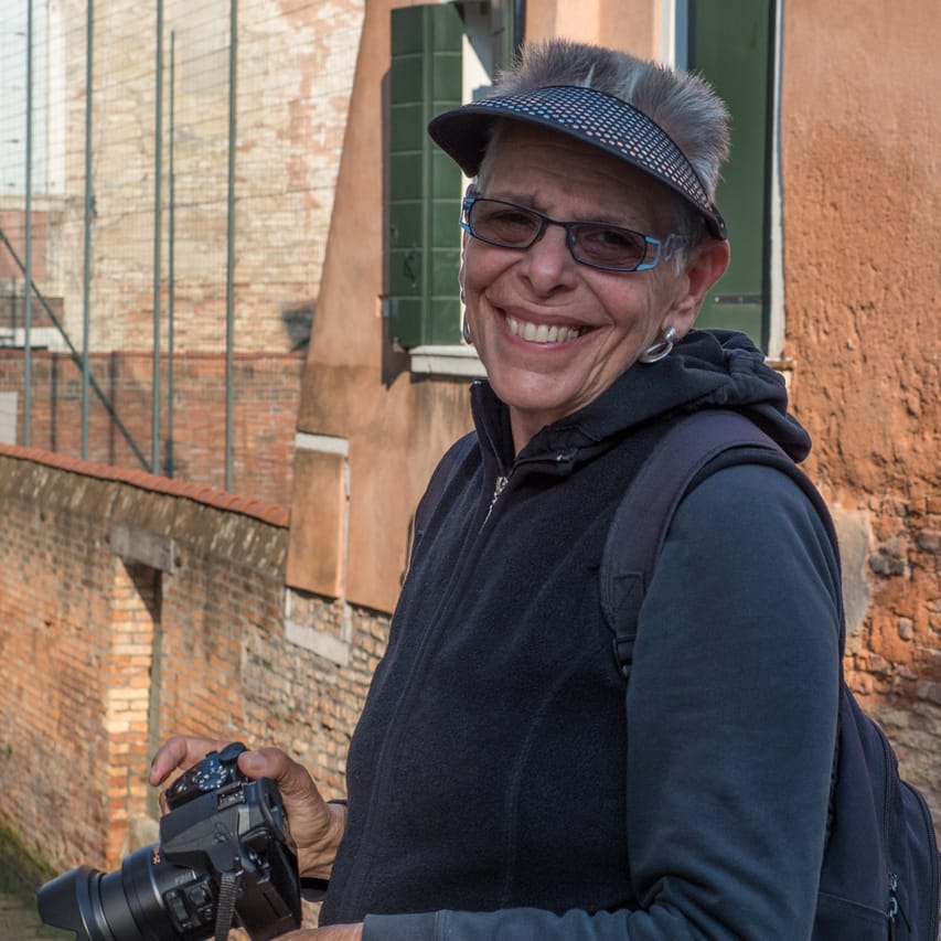 Rita Florea smiling in front of a scenic building holding her camera